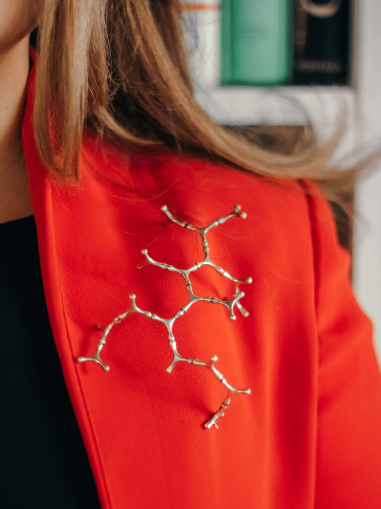 Silver coral branch brooch pinned to a red jacket, detail photography by Sogand Nobahar