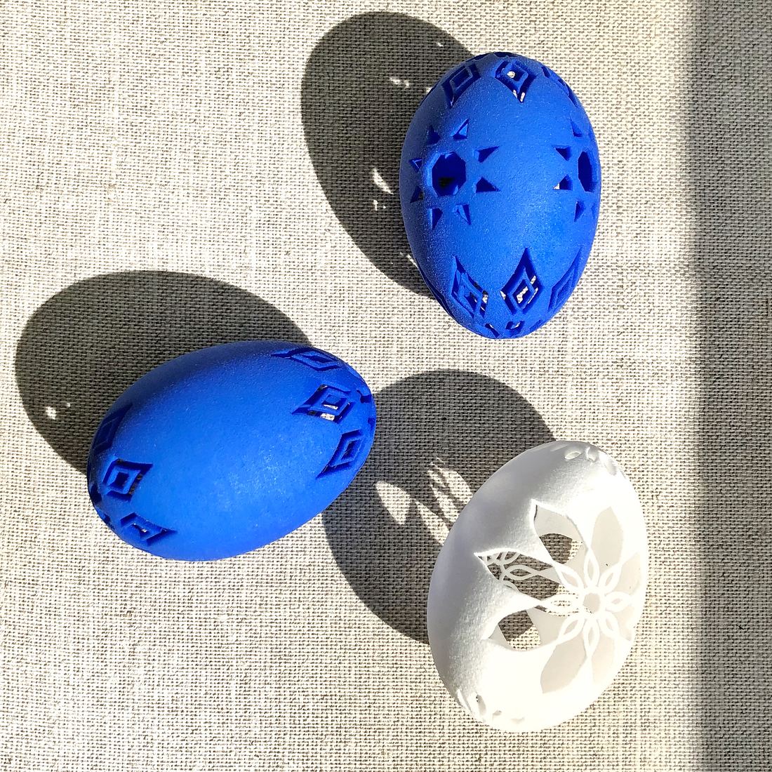 Photograph of the same three 3D printed Nowrouz eggs on linen in direct sunlight