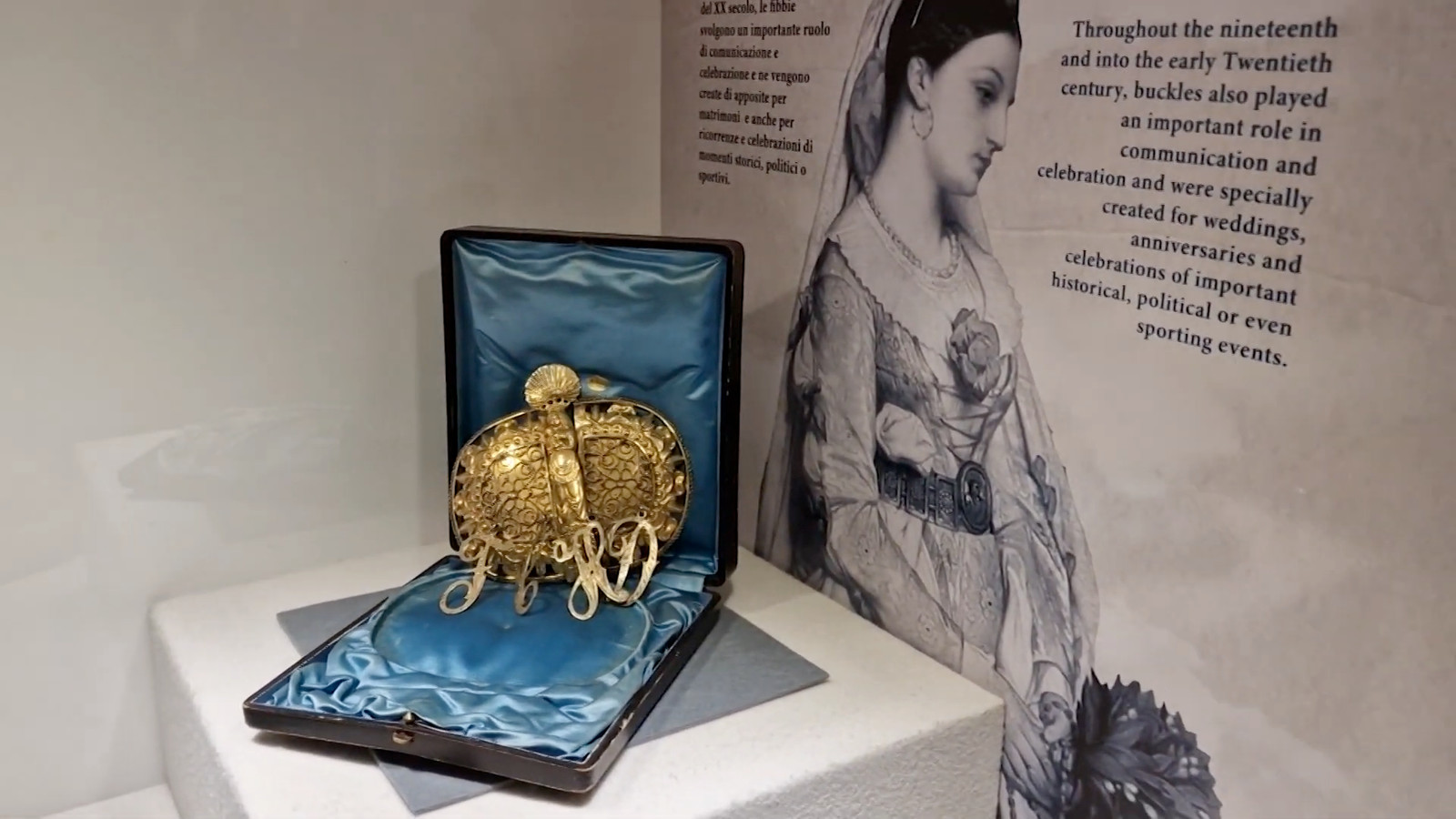 Gold filigree buckle in its original case on a museum cube in front of a collage panel, Milleuna Fibbia