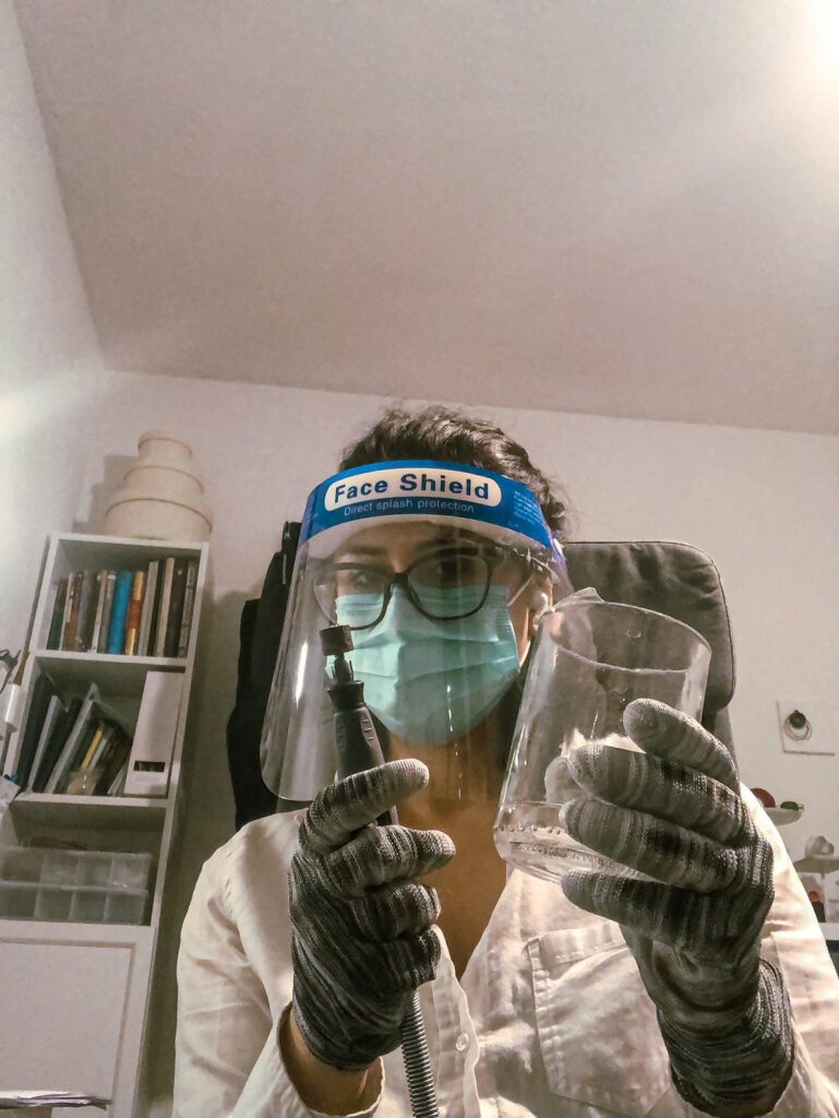 Sogand Nobahar cutting a recovered glass bottle wearing a face shield and cut-resistant gloves
