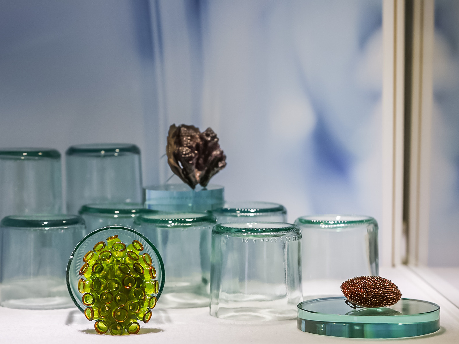 Antique glass jewels displayed on cut recovered bottle bases inside a museum vitrine, exhibition design by Sogand Nobahar for Museo del Bijou di Casalmaggiore