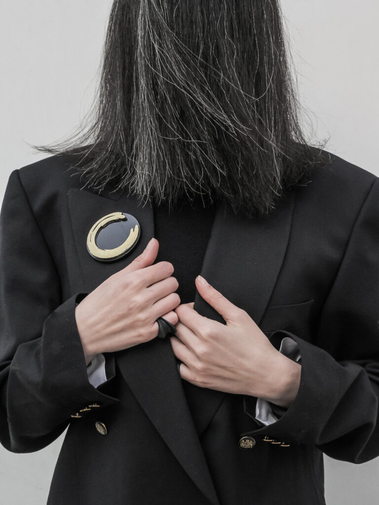 Circular Enso brooch worn on the shoulder of a black blazer, sintered nylon contemporary jewelry by Nobahar Design