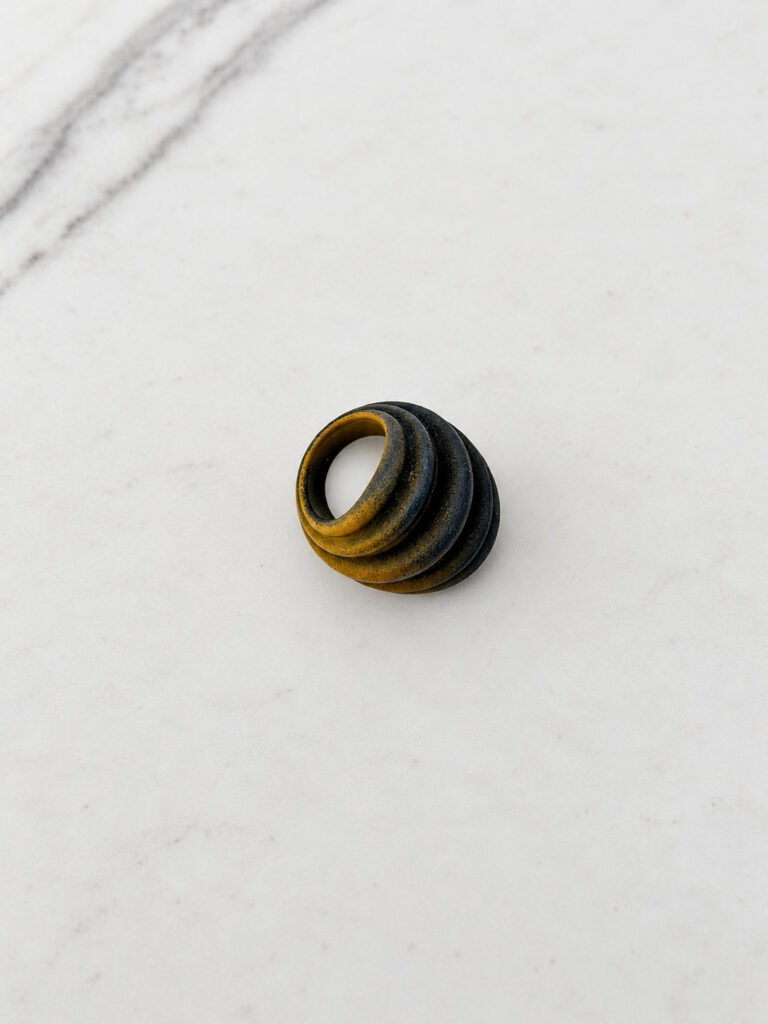 Gold and black sintered nylon ring photographed from above on white marble, small in the frame with nothing to judge its size against